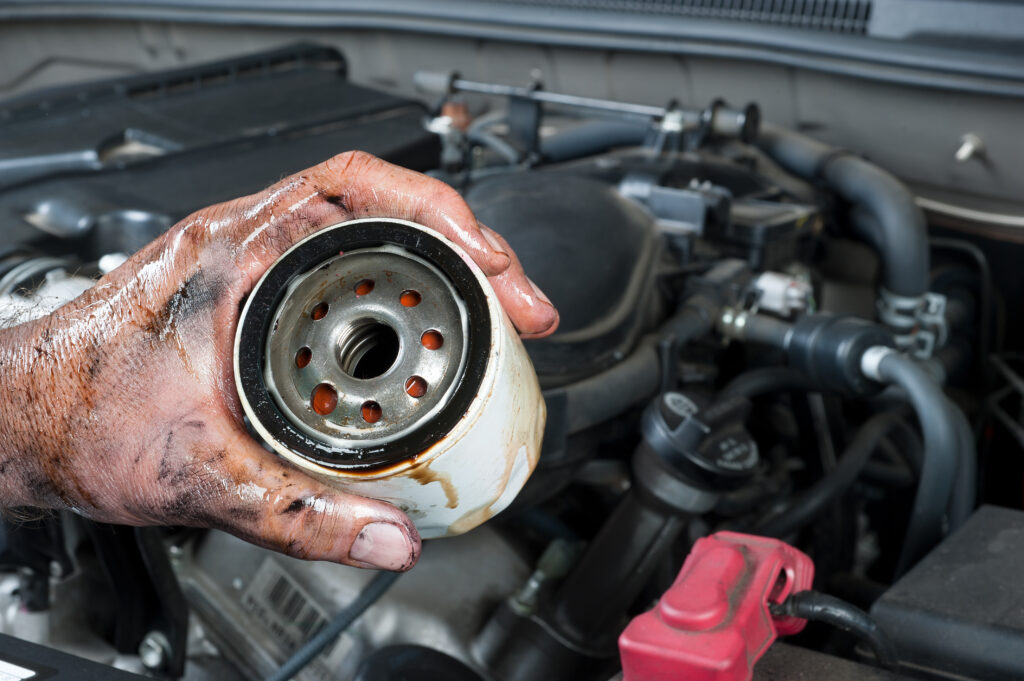 An auto mechanic shows an old, dirty oil filter just removed from a car during general maintenance