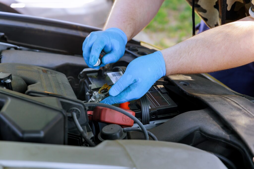 Male mechanic replacement car battery in workshop on car engine background selective focus.